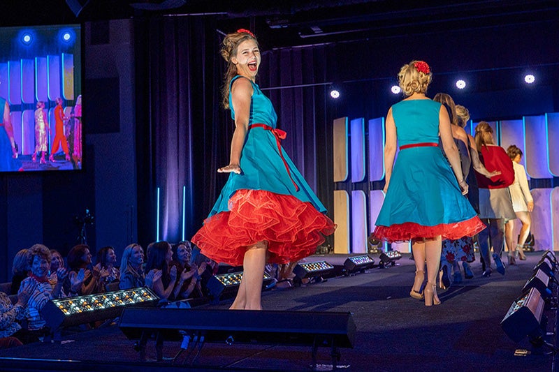 Fashion show model showing off a blue and red dress on the runway.