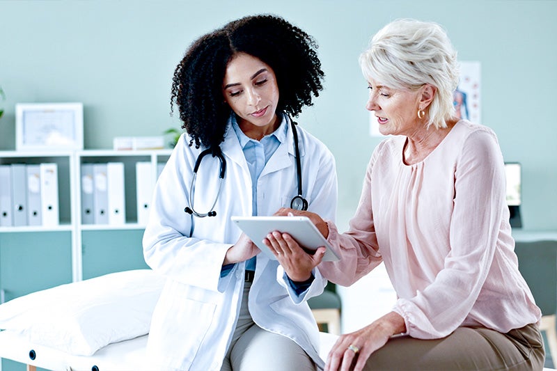 Cardiology specialist speaking with an elderly female patient, while looking at a tablet with test results.